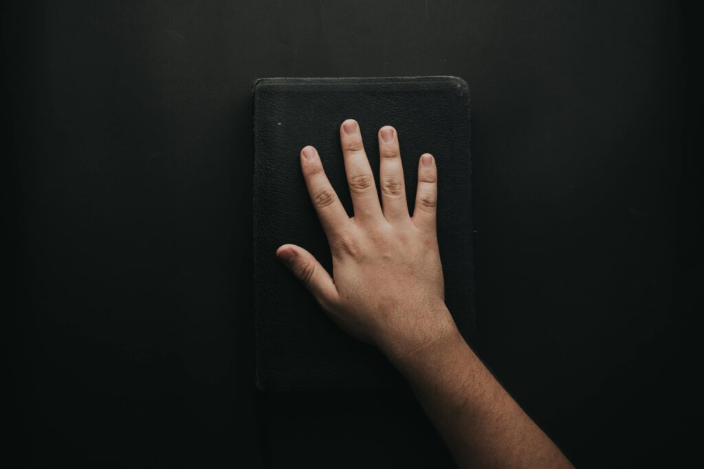 A close-up of a hand resting on a black book against a dark backdrop.